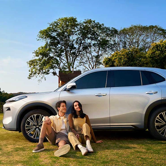Ein Paar sitzt an einen Reifen eines Geely Auto angelehnt.