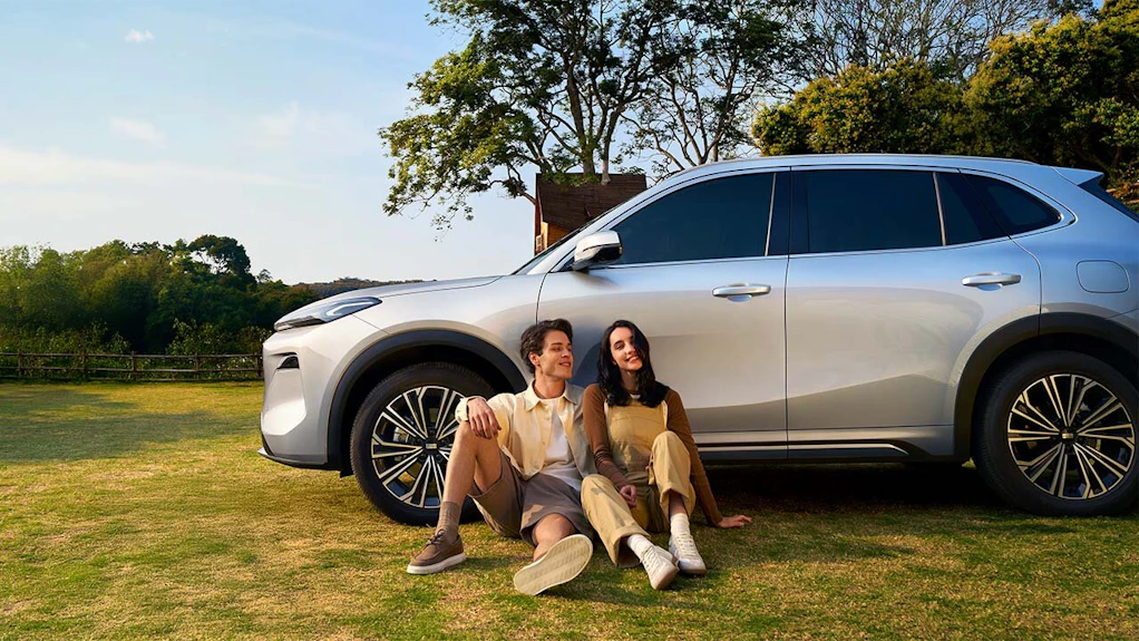 Ein Paar sitzt an einen Reifen eines Geely Auto angelehnt.