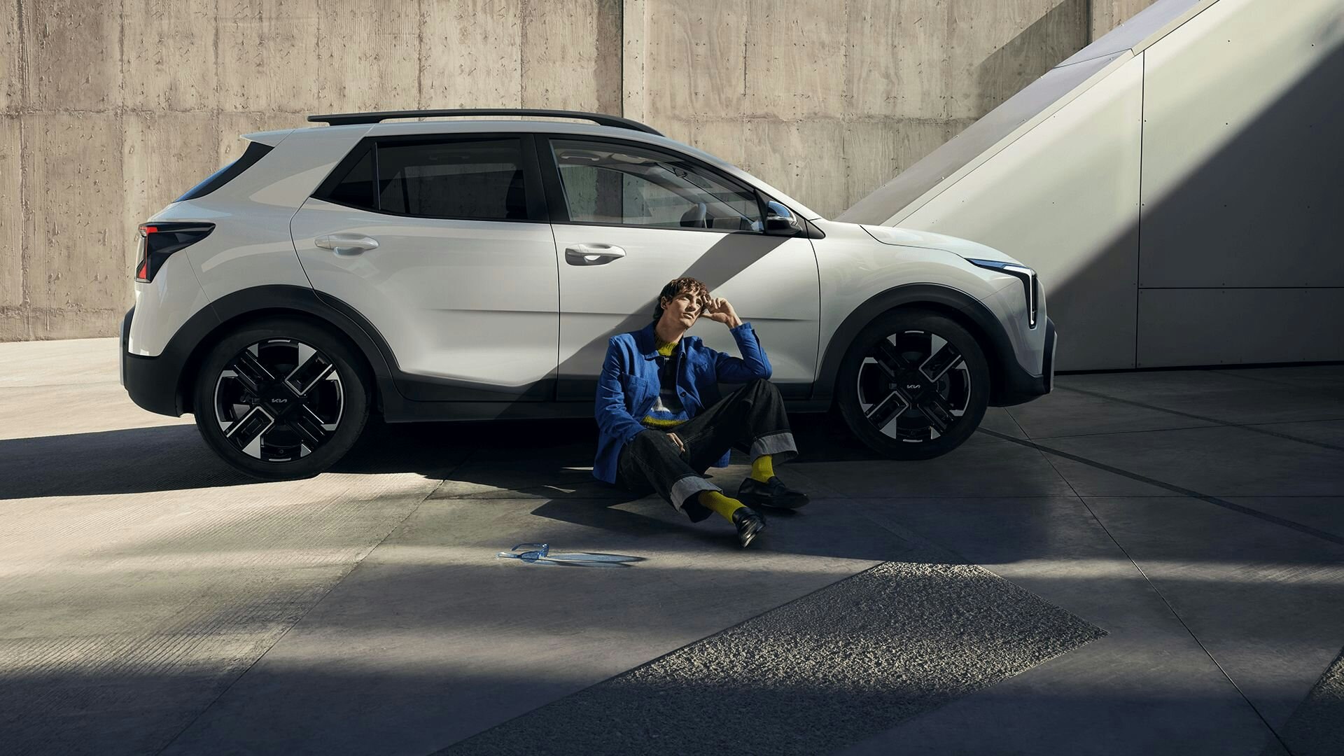 Ein Mann sitzt am Boden und lehnt sich an neuen Kia Stonic in weiss