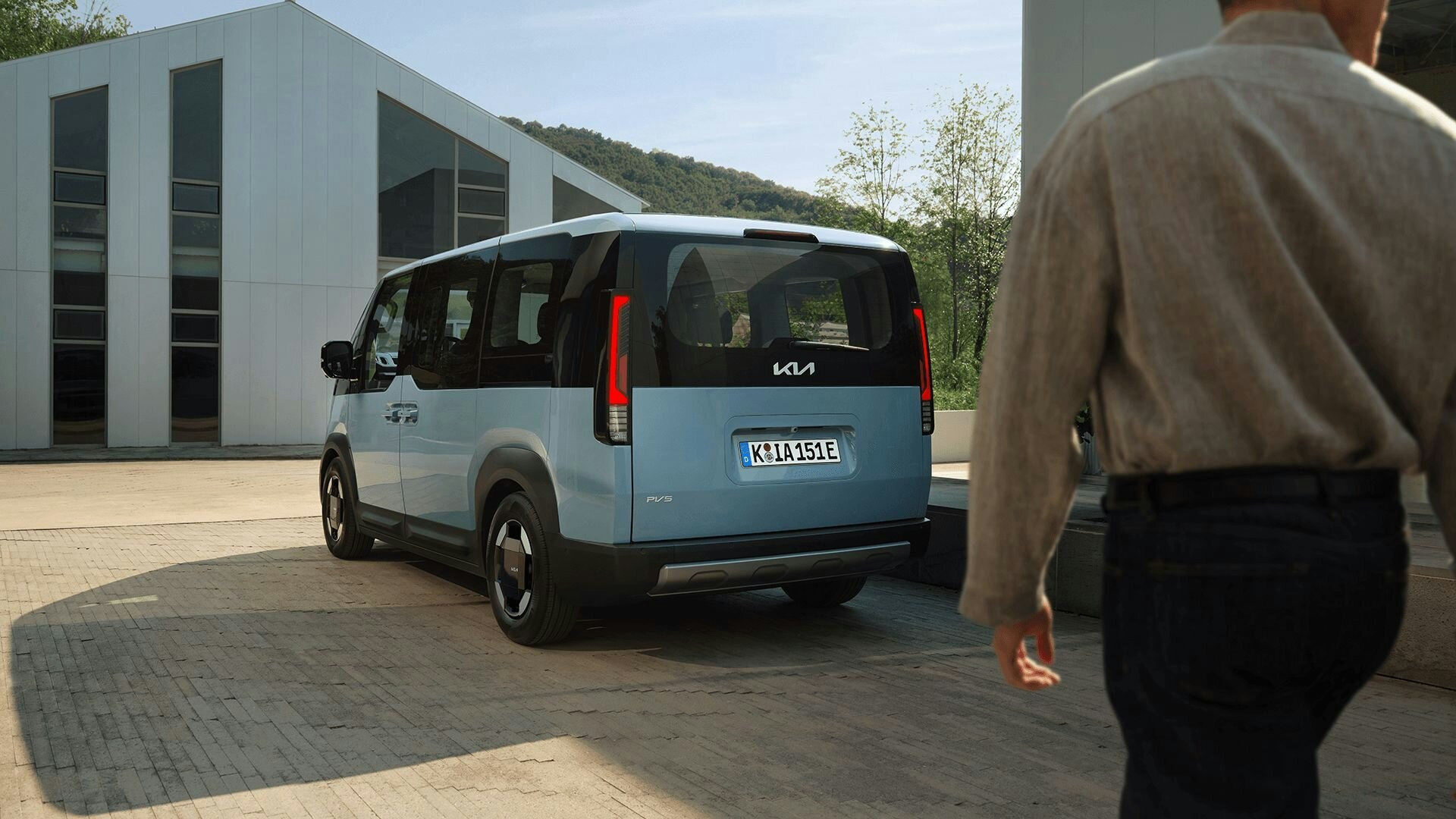 Frontansicht des Kia PV5 Passenger bei der Fahrt durch eine städtische Küstenregion