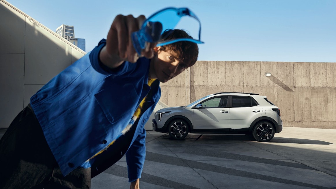 Un homme tient une paire de lunettes face à la caméra devant la nouvelle Kia Stonic