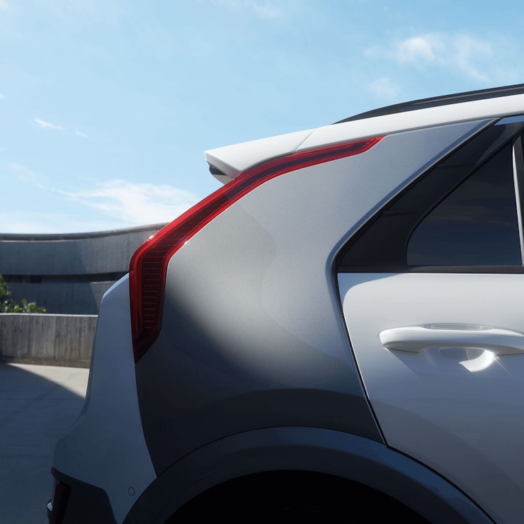 Eine Frau steht angelehnt am Kia Niro