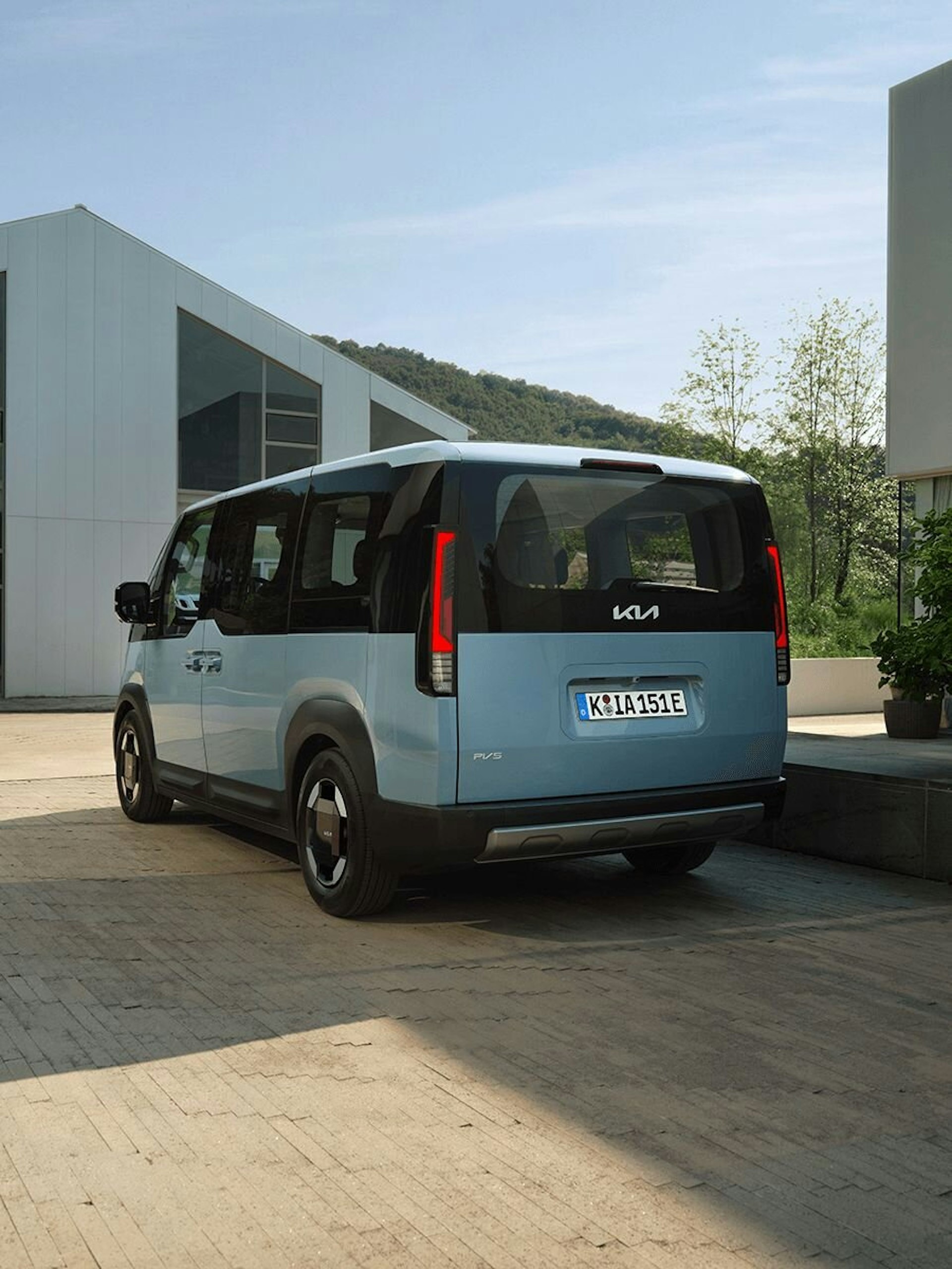 Frontansicht des Kia PV5 Passenger bei der Fahrt durch eine städtische Küstenregion