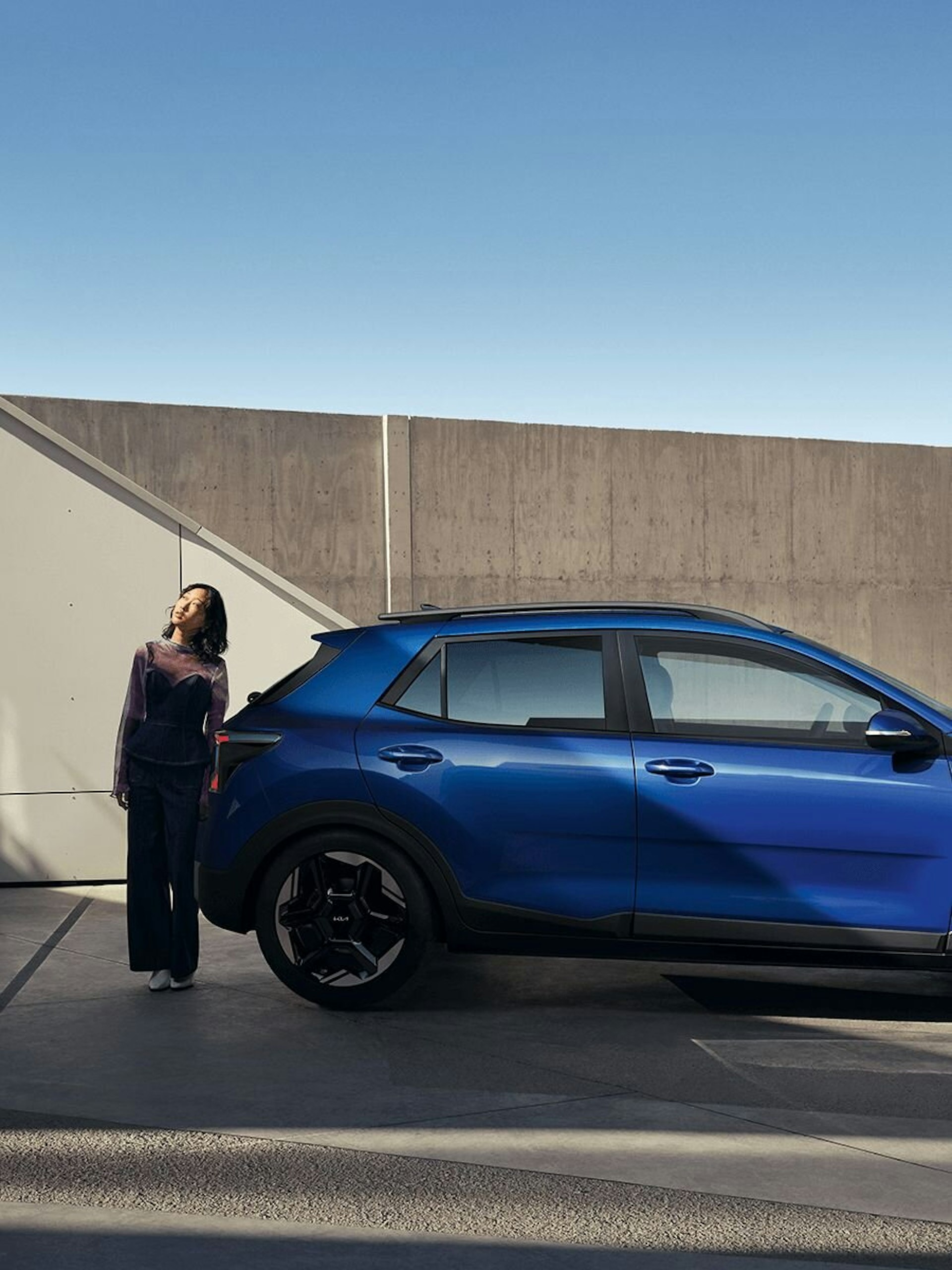 Eine Frau steht hinter dem neuen Kia Stonic und schaut in den Himmel