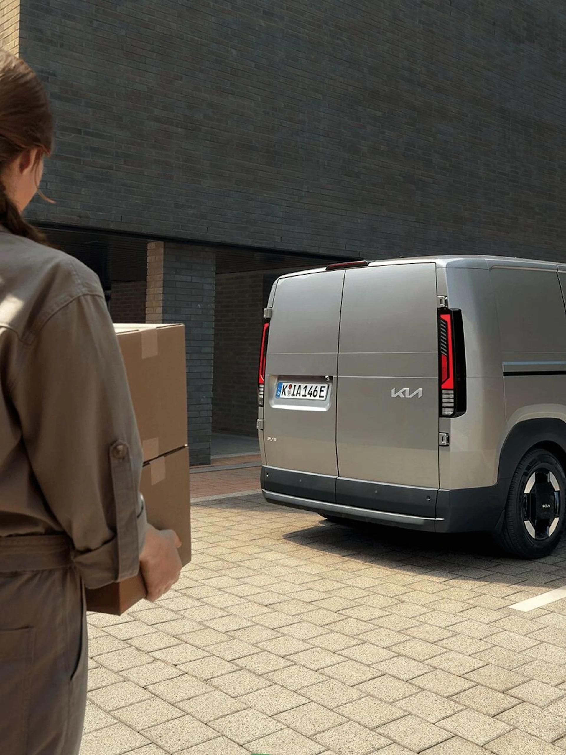 Eine Frau nähert sich mit einem Paket von hinten an den Kia PV5 Cargo an