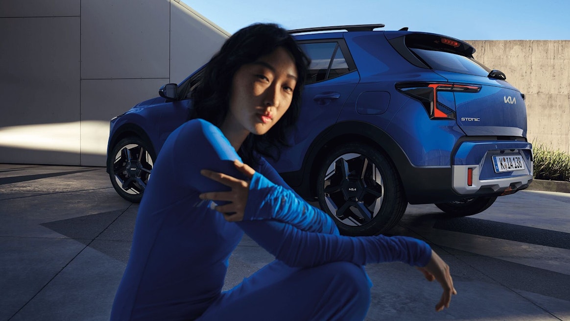 Une femme en robe bleue est assise devant la Kia Stonic bleue